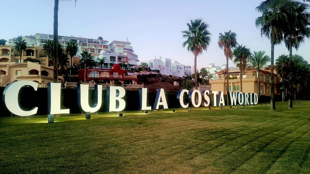 Large “CLUB LA COSTA WORLD” sign on a lawn with palm trees and resort buildings in the background