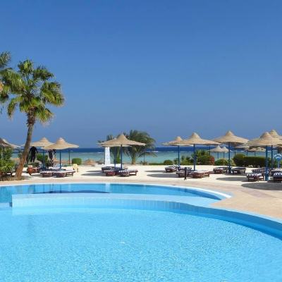 Outdoor resort swimming pool with sun loungers and straw parasols, palm trees and sea view under a clear blue sky