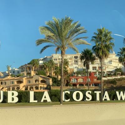 Entrance sign reading “CLUB LA COSTA WORLD” in front of a palm-lined resort complex under a clear blue sky